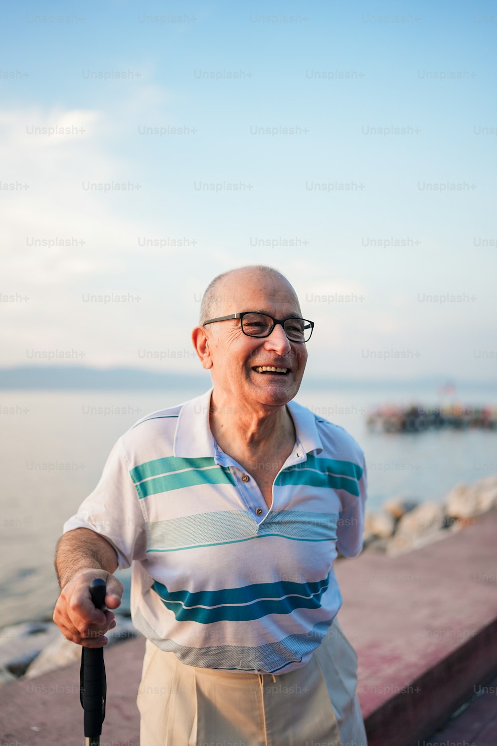 Ein älterer Mann, der einen Regenschirm in der Nähe des Wassers hält