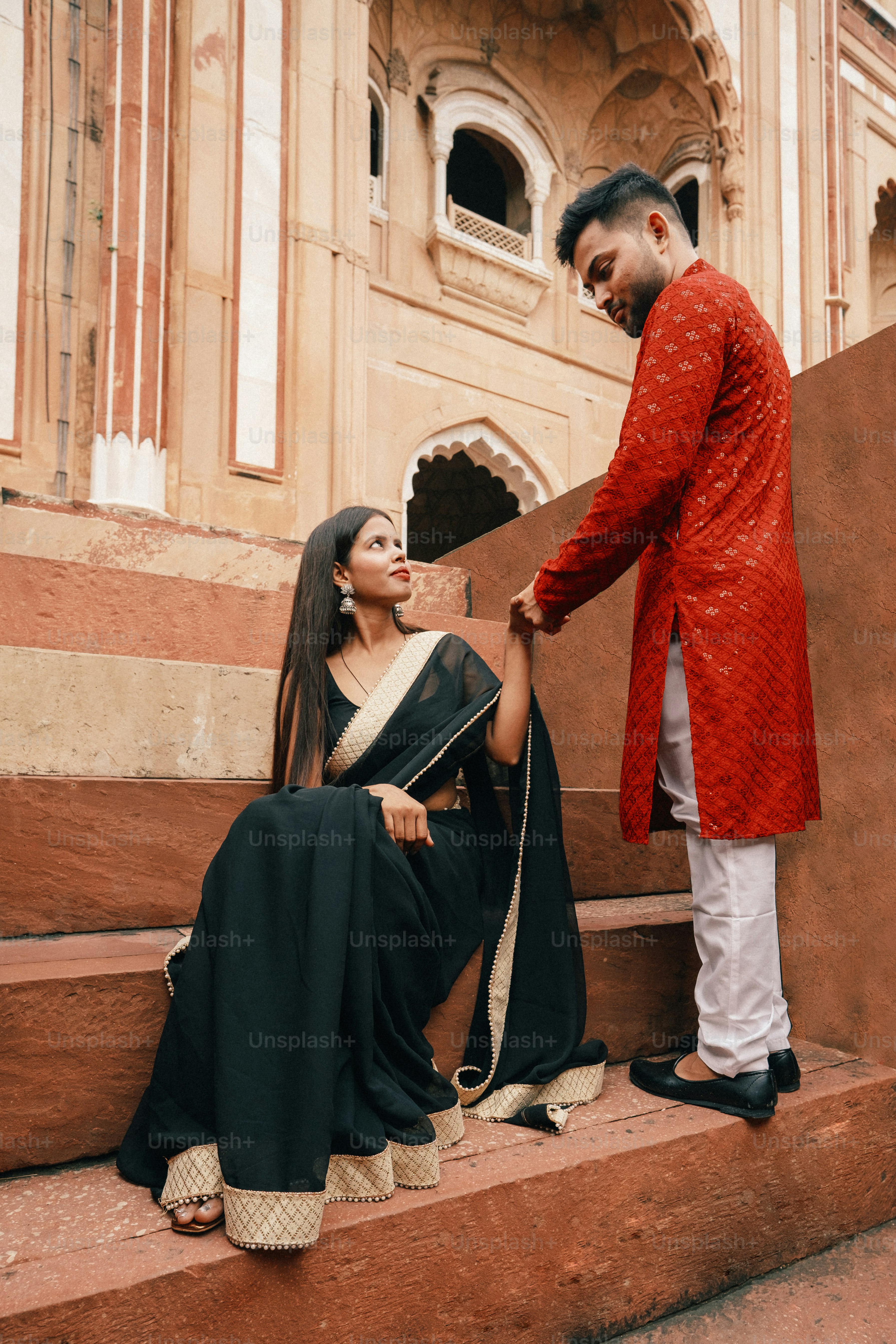 a man in a red jacket standing next to a woman in a black sari
