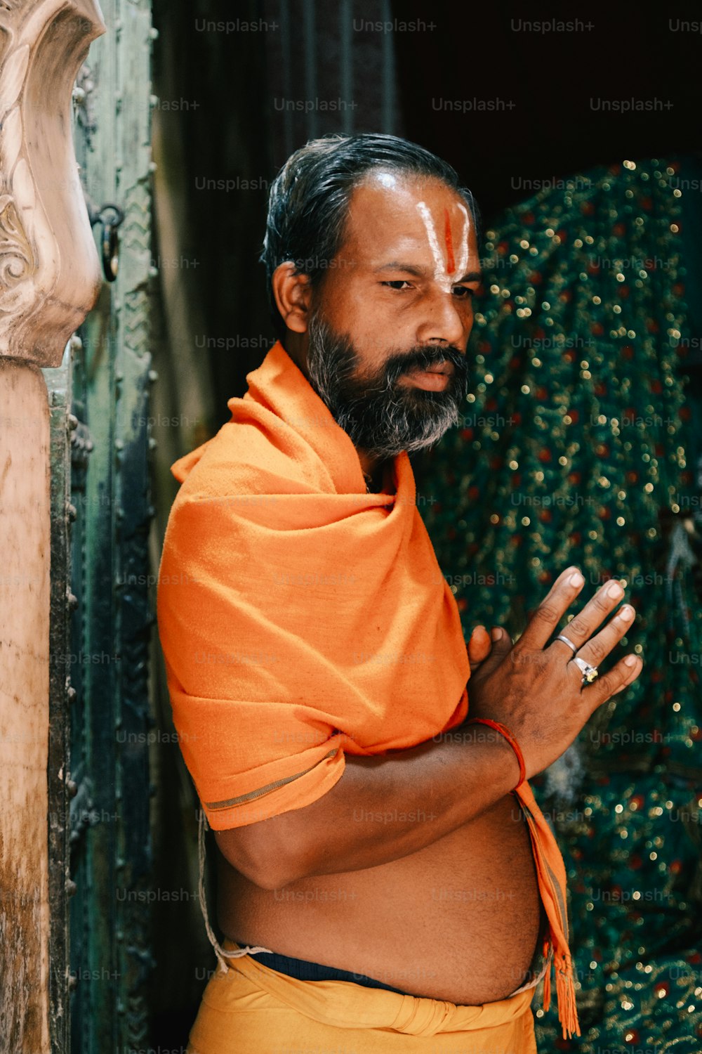 a man wearing an orange shawl standing in front of a doorway