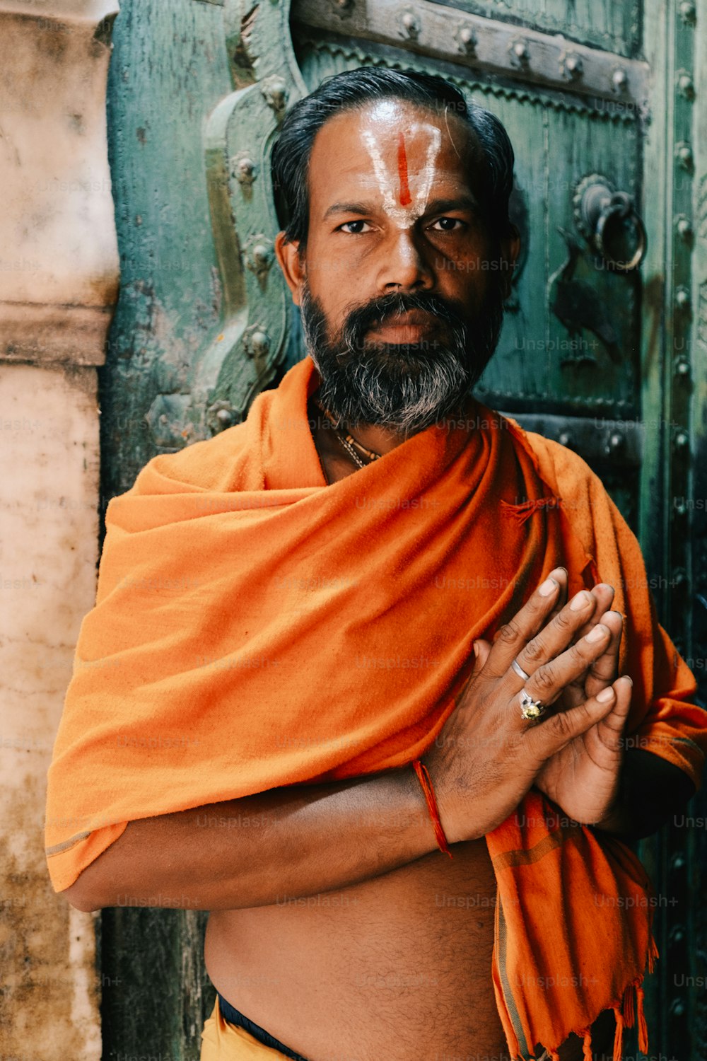 a man wearing an orange shawl standing in front of a door