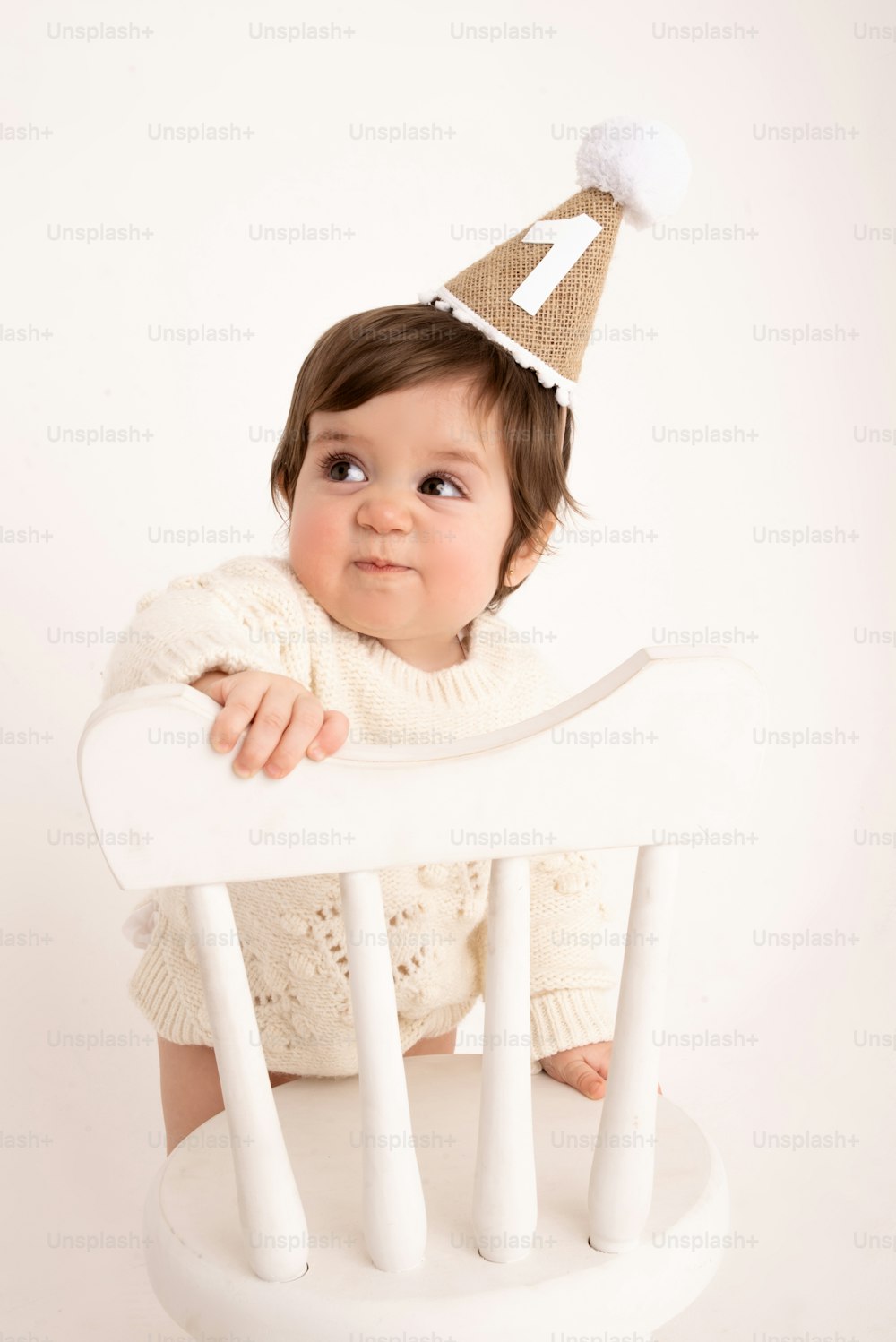 a baby wearing a birthday hat sitting in a chair