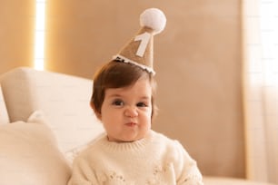 a baby wearing a birthday hat sitting on a couch