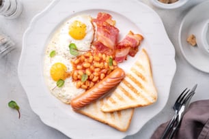 um prato branco coberto com ovos, bacon, feijão e torradas