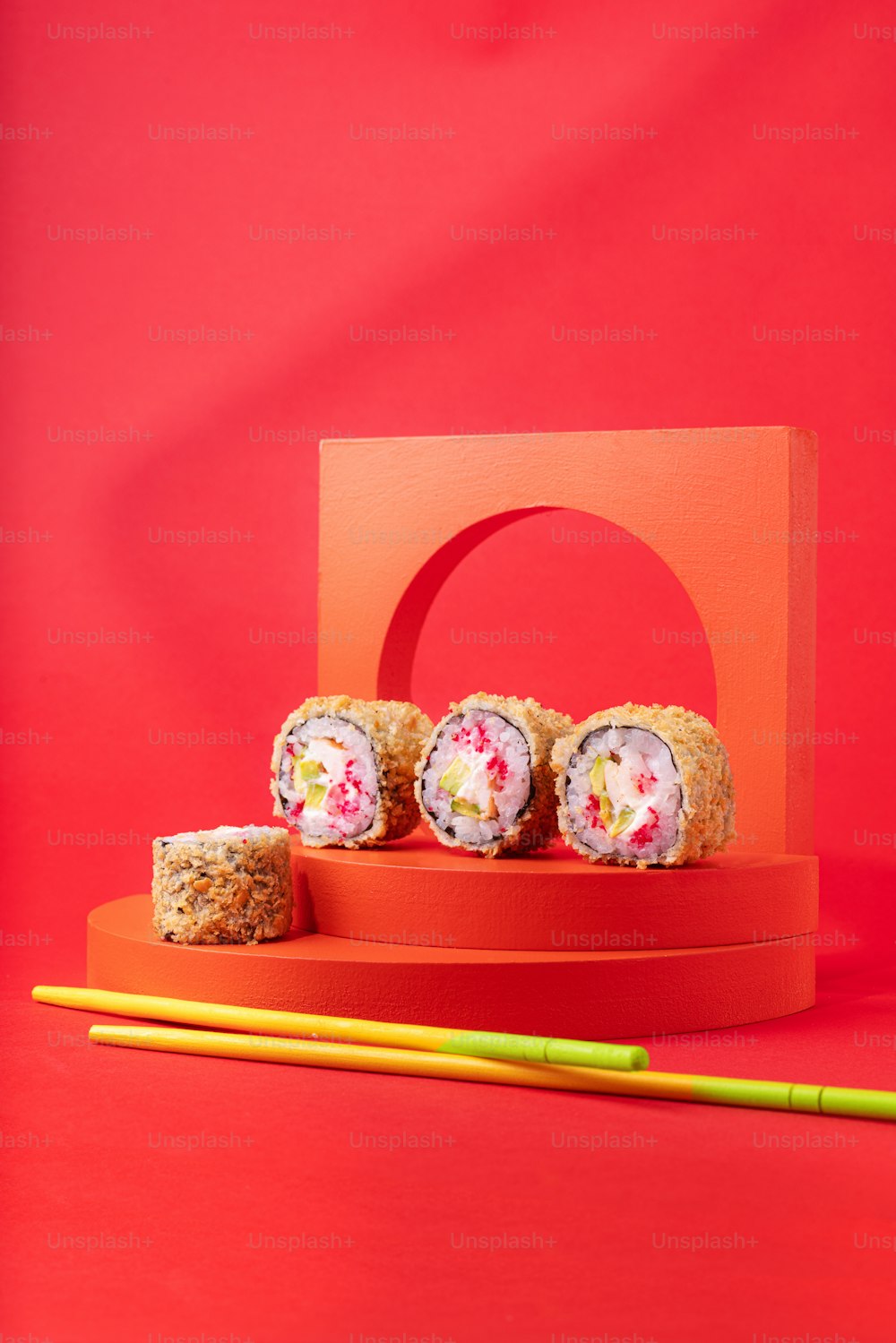 three sushi rolls on a red plate with chopsticks