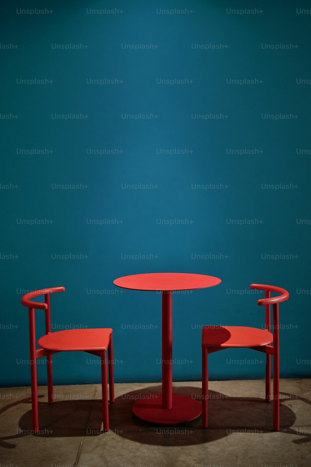 uma mesa vermelha e duas cadeiras contra uma parede azul