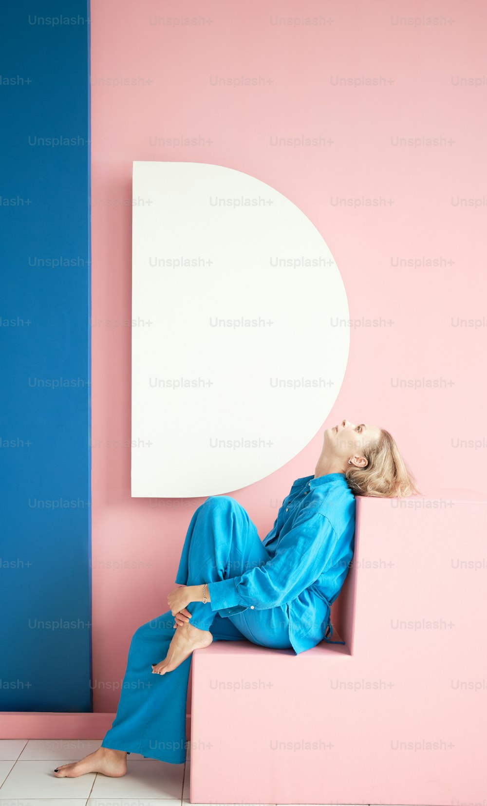 a woman sitting on top of a pink and blue wall