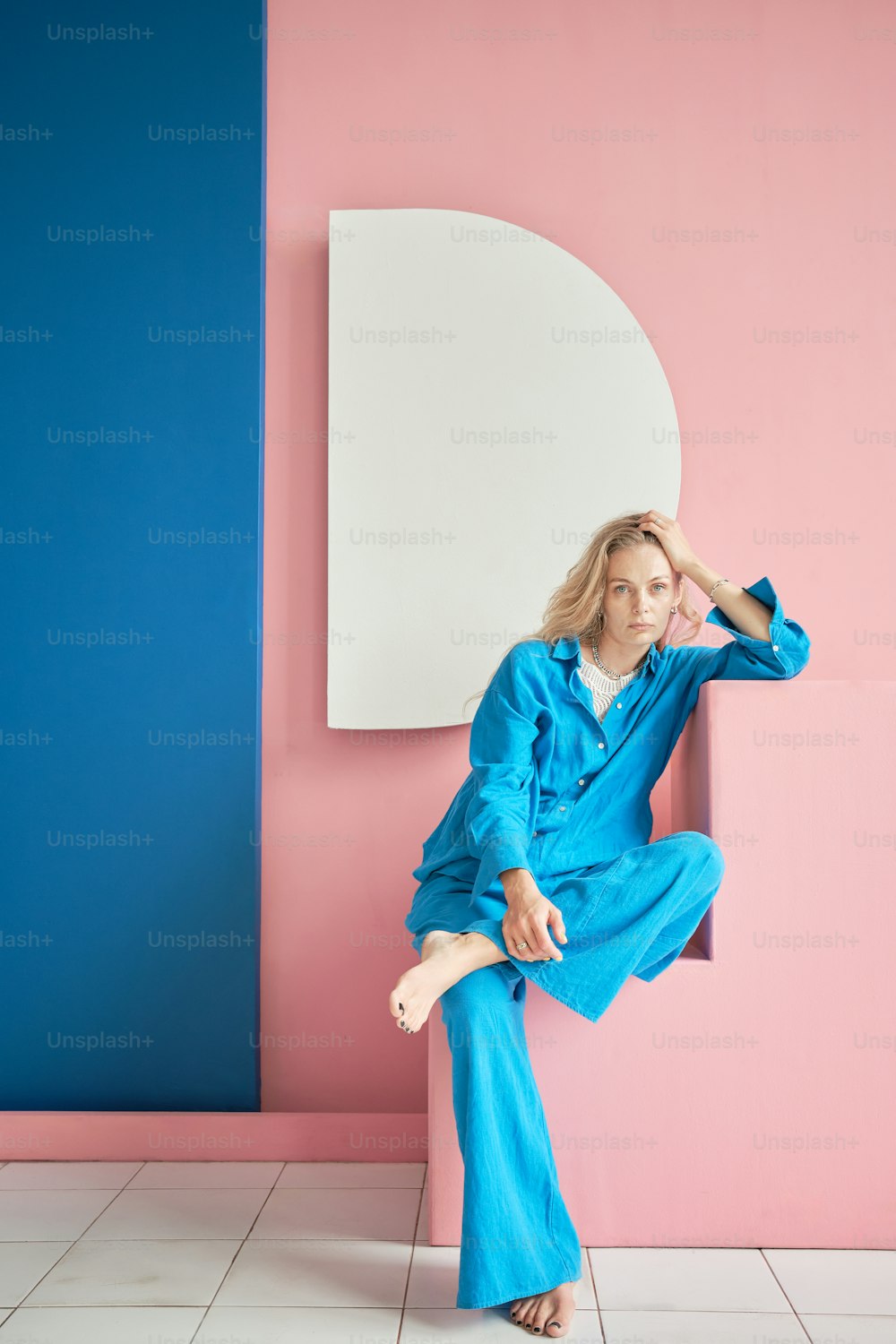 a woman in a blue jumpsuit sitting on a pink and blue wall