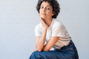 a woman sitting on a stool with her chin resting on her hand