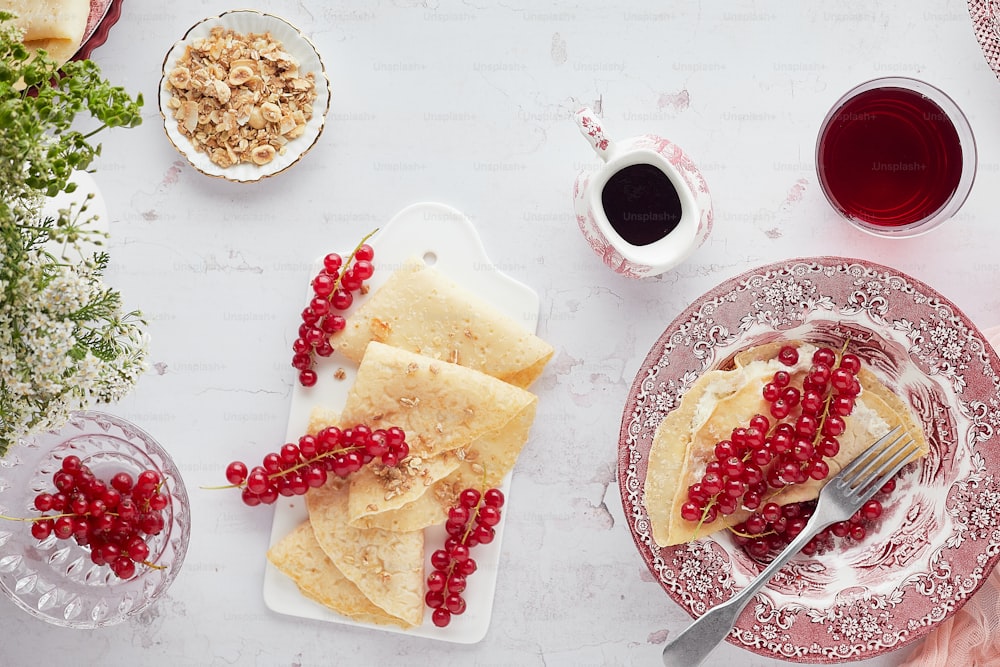 a plate of crepes with red berries and a cup of coffee