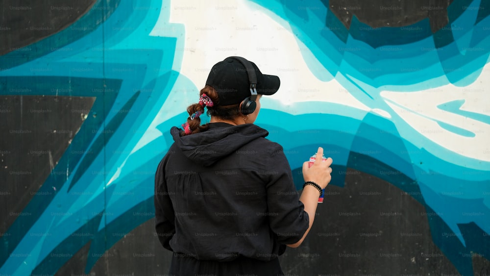 eine Person mit Kopfhörern und Kapuzenpullover, die vor einer Graffiti-Wand steht