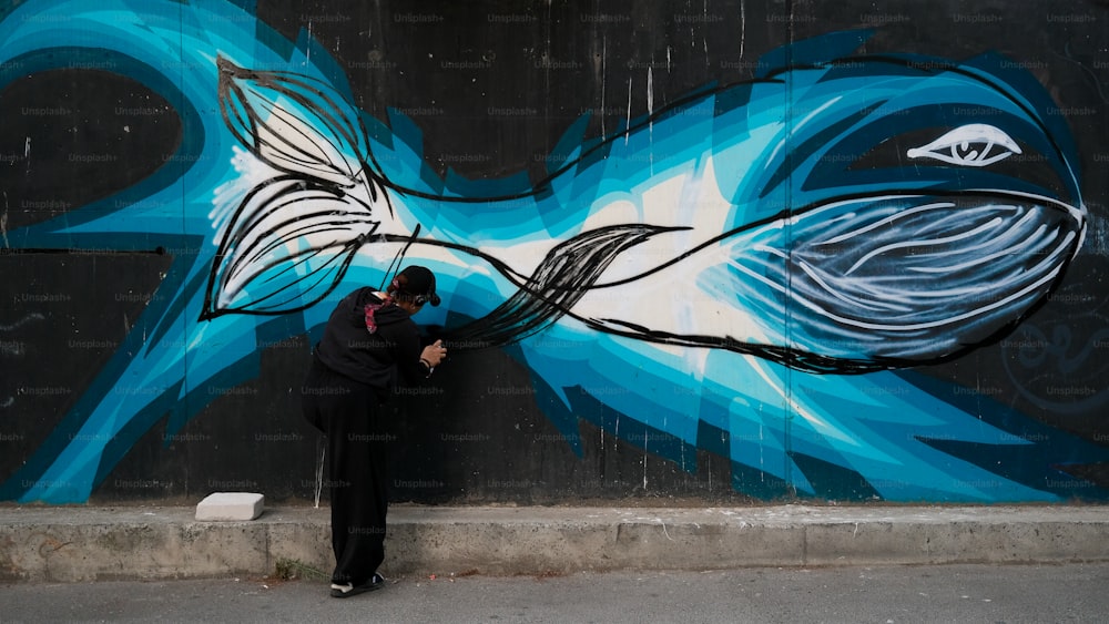 um homem pintando um peixe na lateral de um prédio