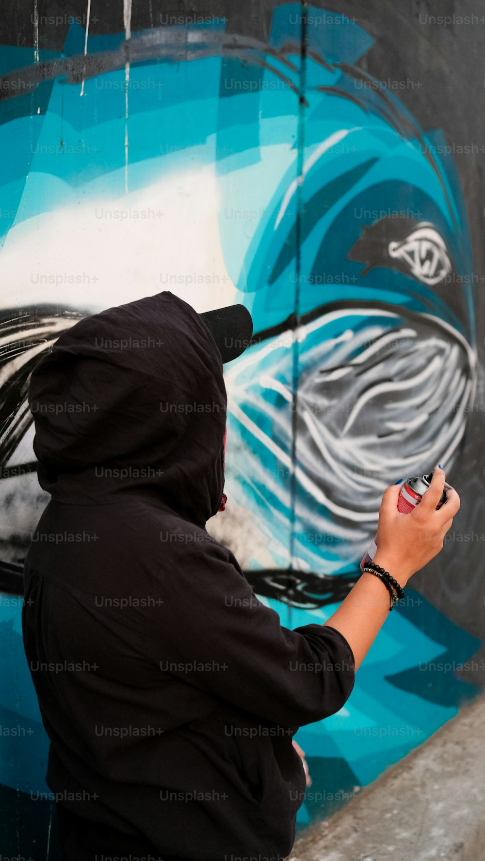 Une personne vêtue d’un sweat à capuche noir peint une peinture murale