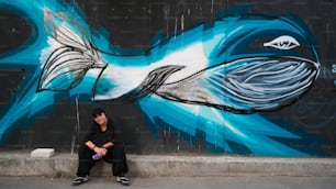 a man sitting in front of a painting of a fish