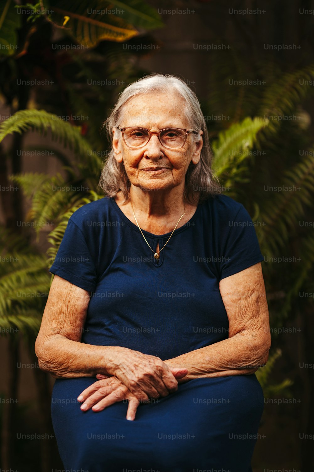 Una donna anziana con gli occhiali seduta di fronte a una pianta