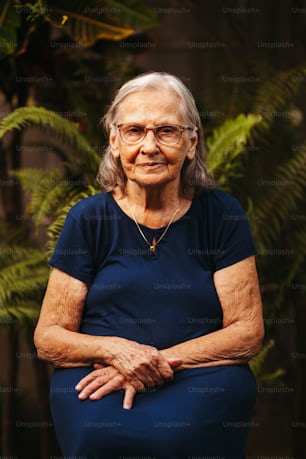 an older woman with glasses sitting in front of a plant