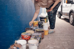 a woman leaning over a blue wall picking up paint