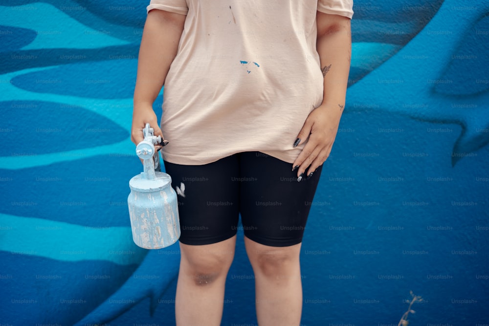 uma mulher em pé na frente de uma parede azul segurando uma garrafa de água