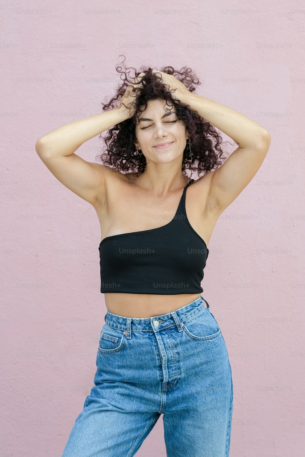 a woman with curly hair wearing jeans and a crop top