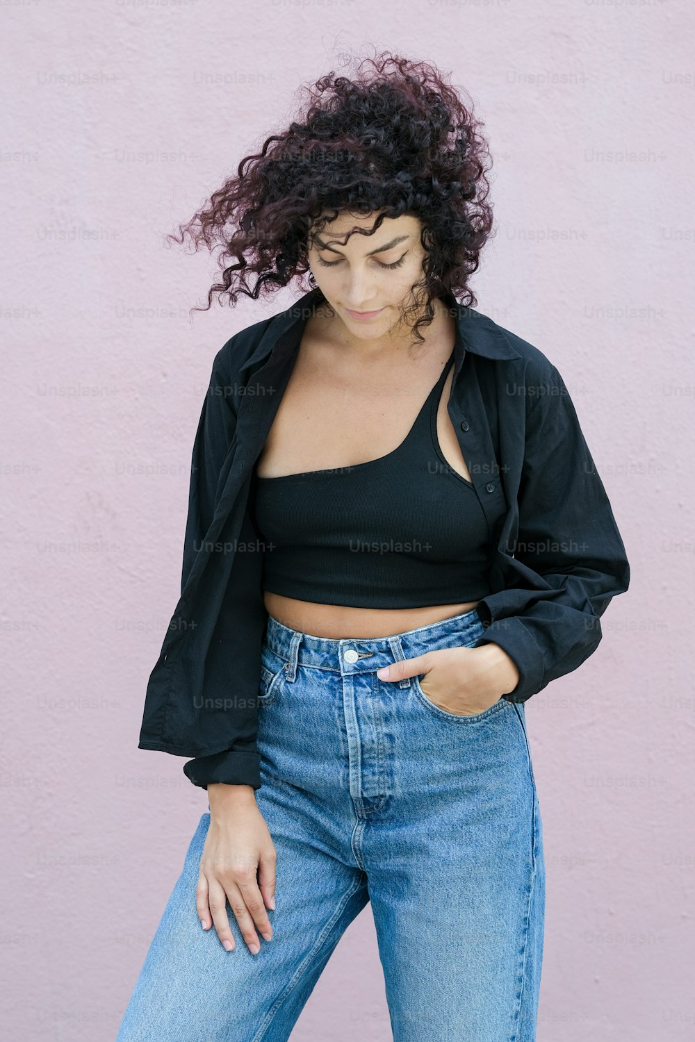 a woman with curly hair wearing jeans and a crop top