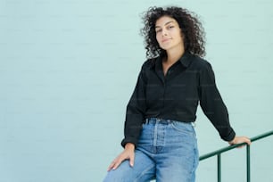 a woman in a black shirt and jeans leaning on a rail