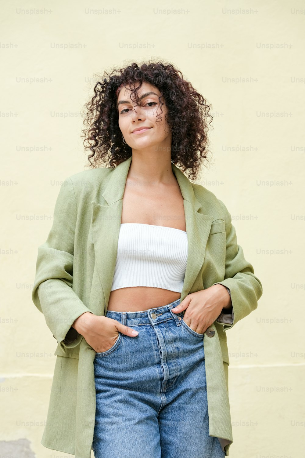 a woman with curly hair wearing a green jacket and jeans