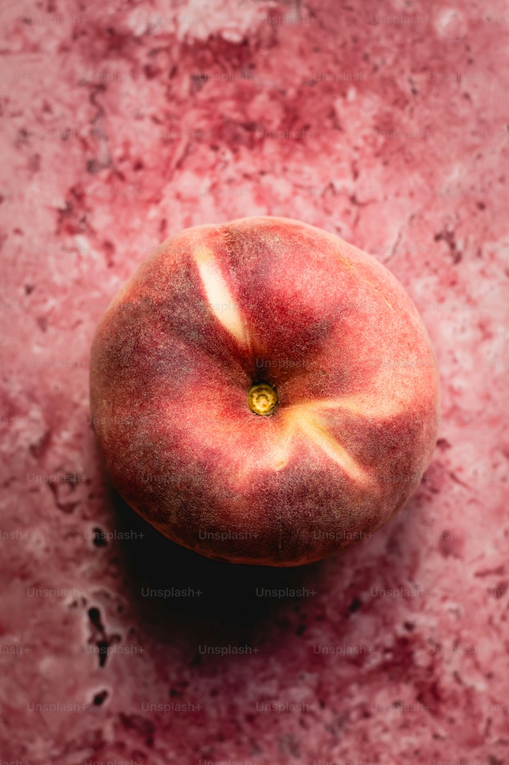 a peach sitting on top of a pink surface