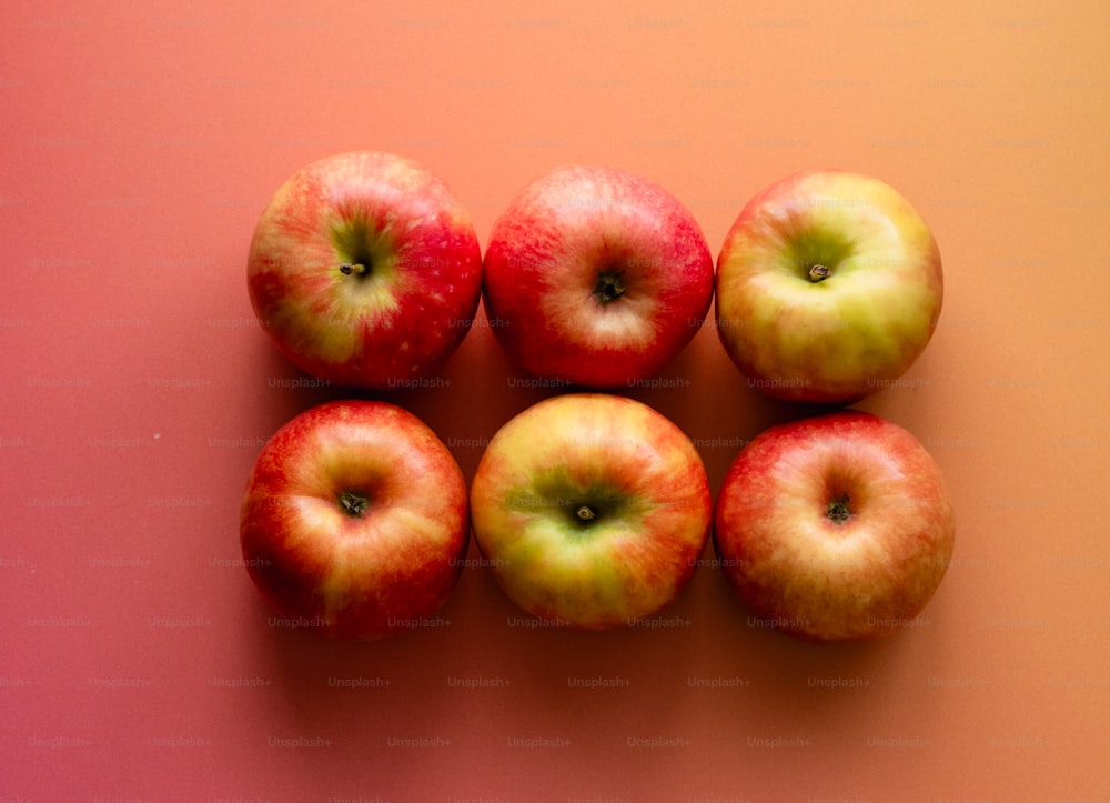 a group of five apples sitting on top of a pink surface