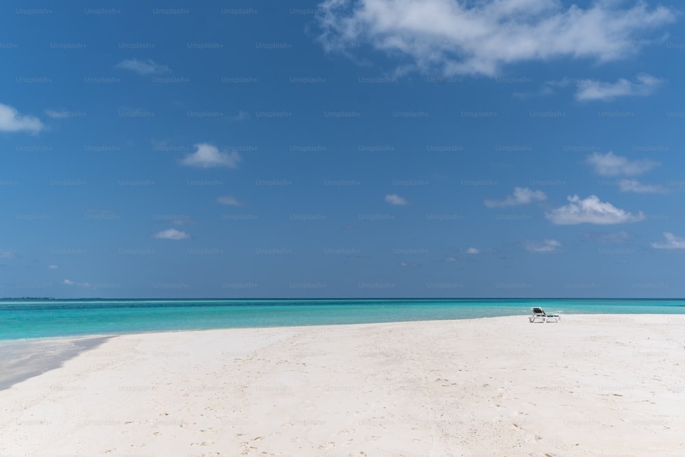 une plage de sable avec une eau bleue claire et des nuages