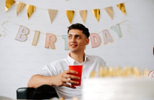 um homem segurando um copo vermelho na frente de um bolo de aniversário