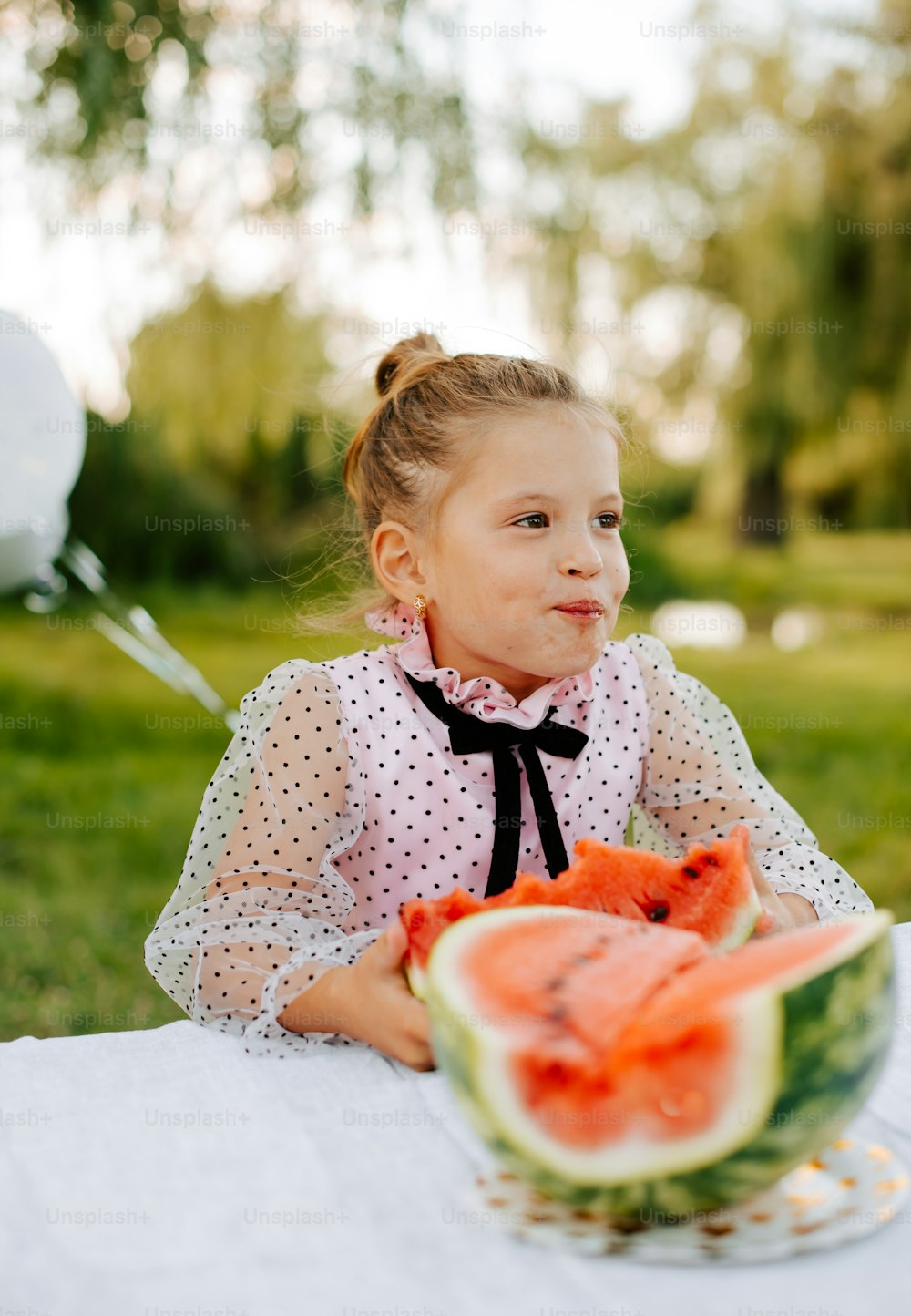 a little girl sitting at a table with a slice of watermelon