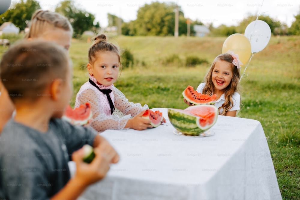 a group of children sitting at a table with watermelon slices