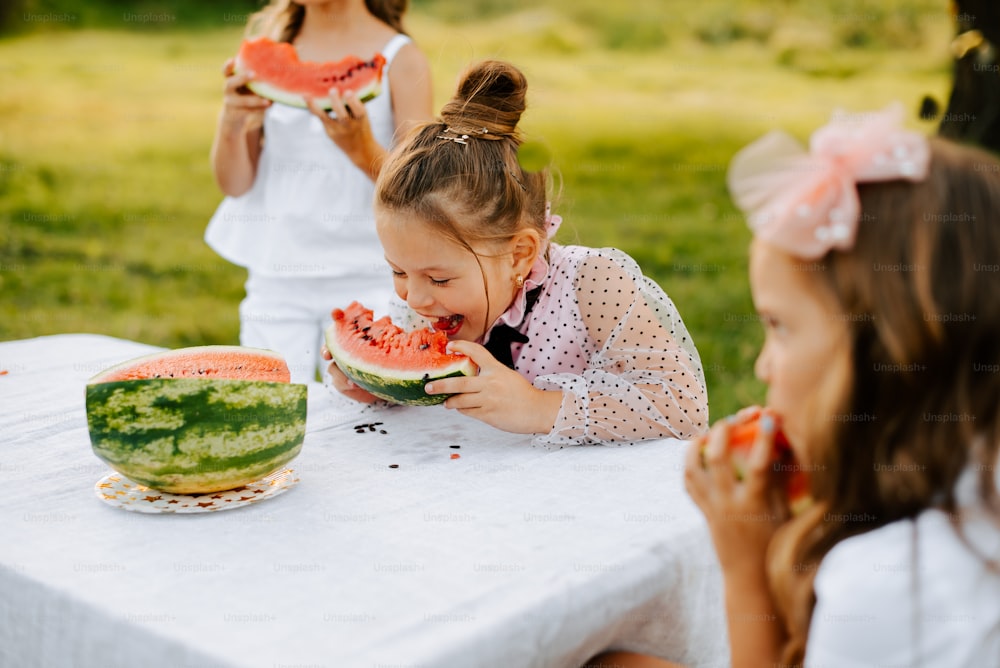 Una niña comiendo una rodaja de sandía en una mesa
