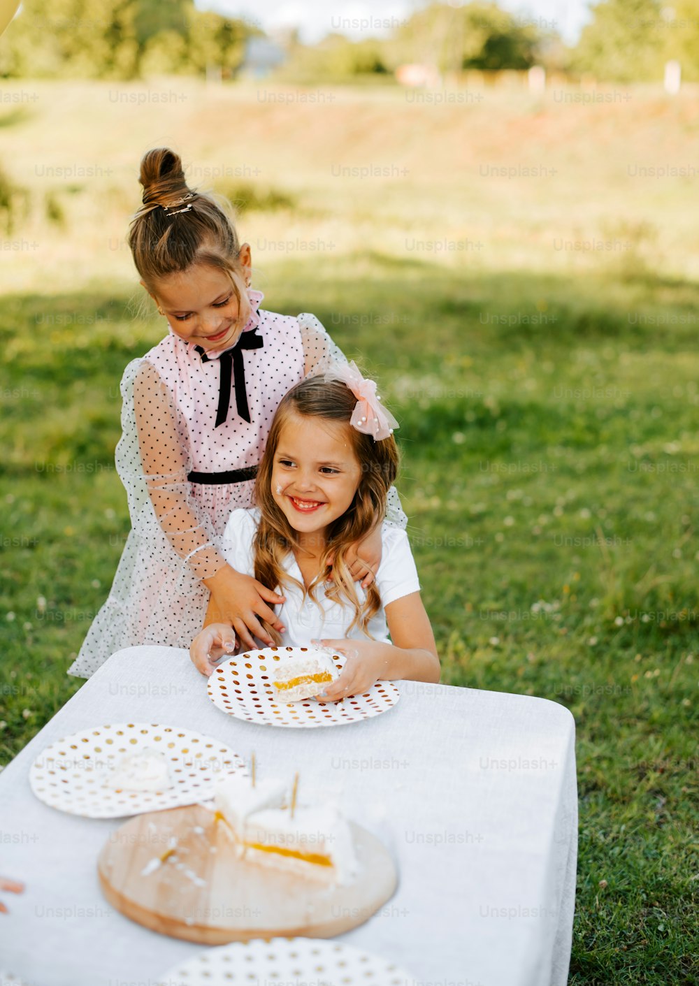 two little girls sitting at a table with a piece of cake