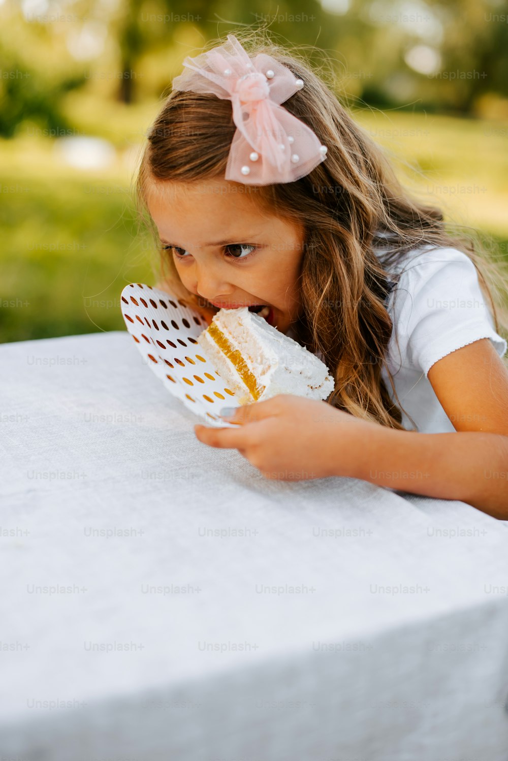 a little girl sitting at a table eating a piece of cake