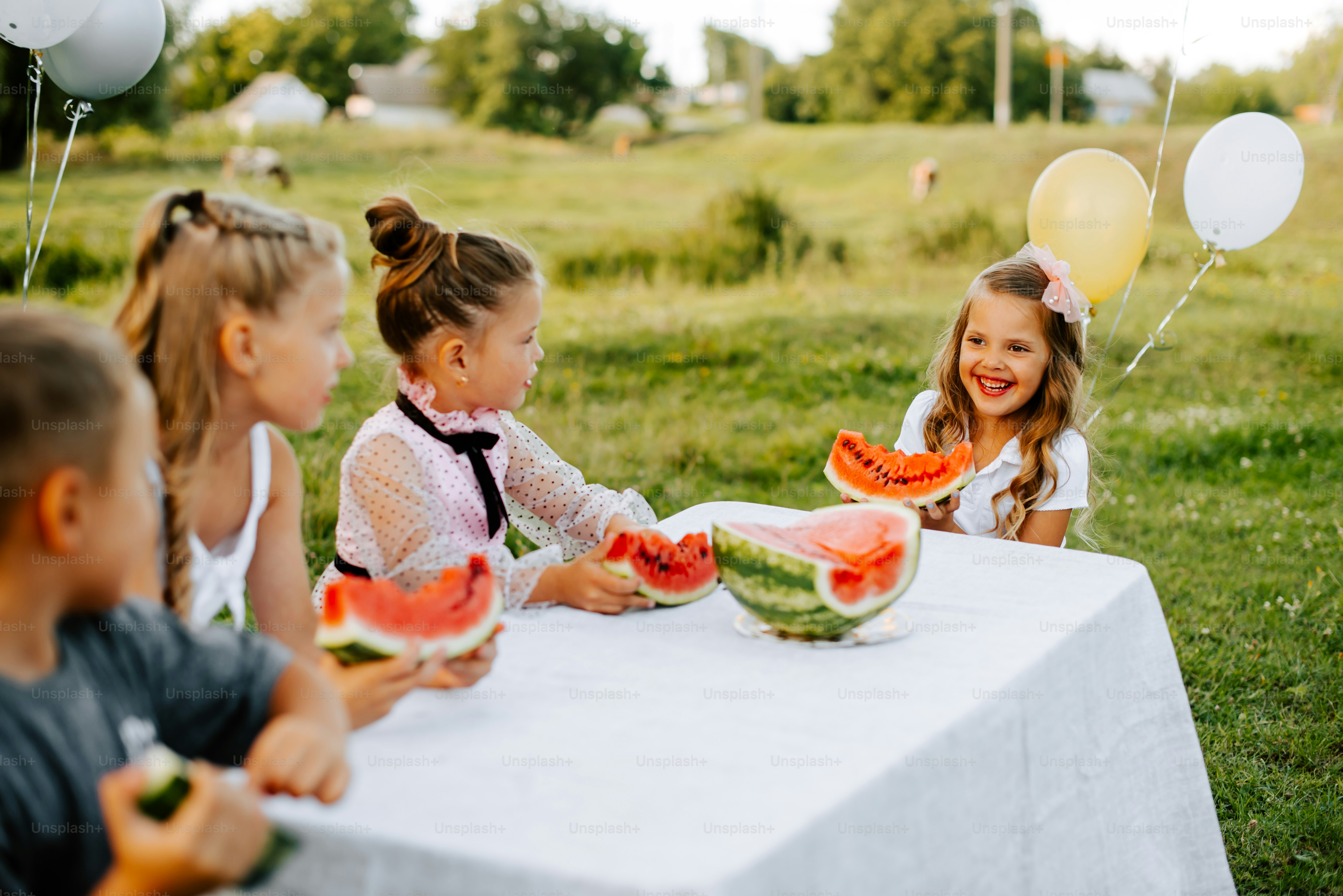 a group of children sitting at a table eating watermelon