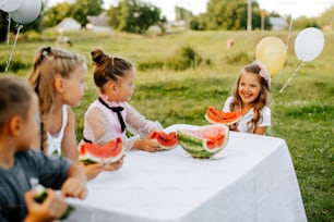 a group of children sitting at a table eating watermelon