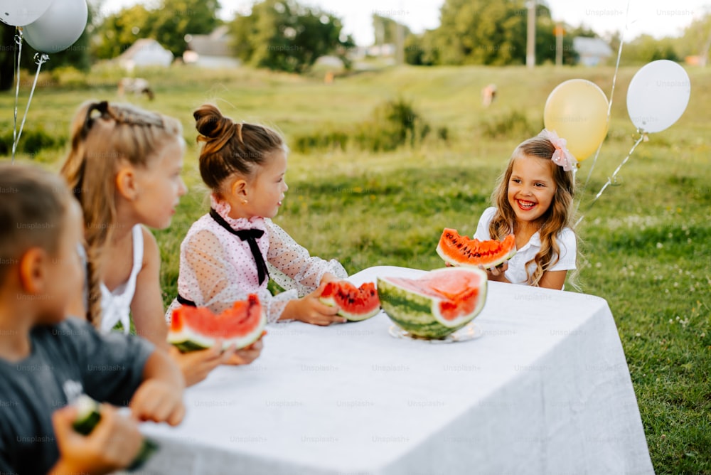 a group of children sitting at a table eating watermelon