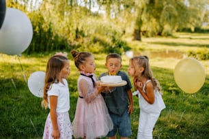 a group of young children standing around a cake