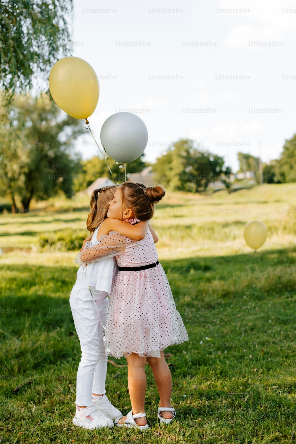 two little girls hugging each other in a field with balloons