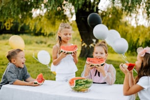 Eine Gruppe von Kindern, die um einen Tisch sitzen und Wassermelone essen