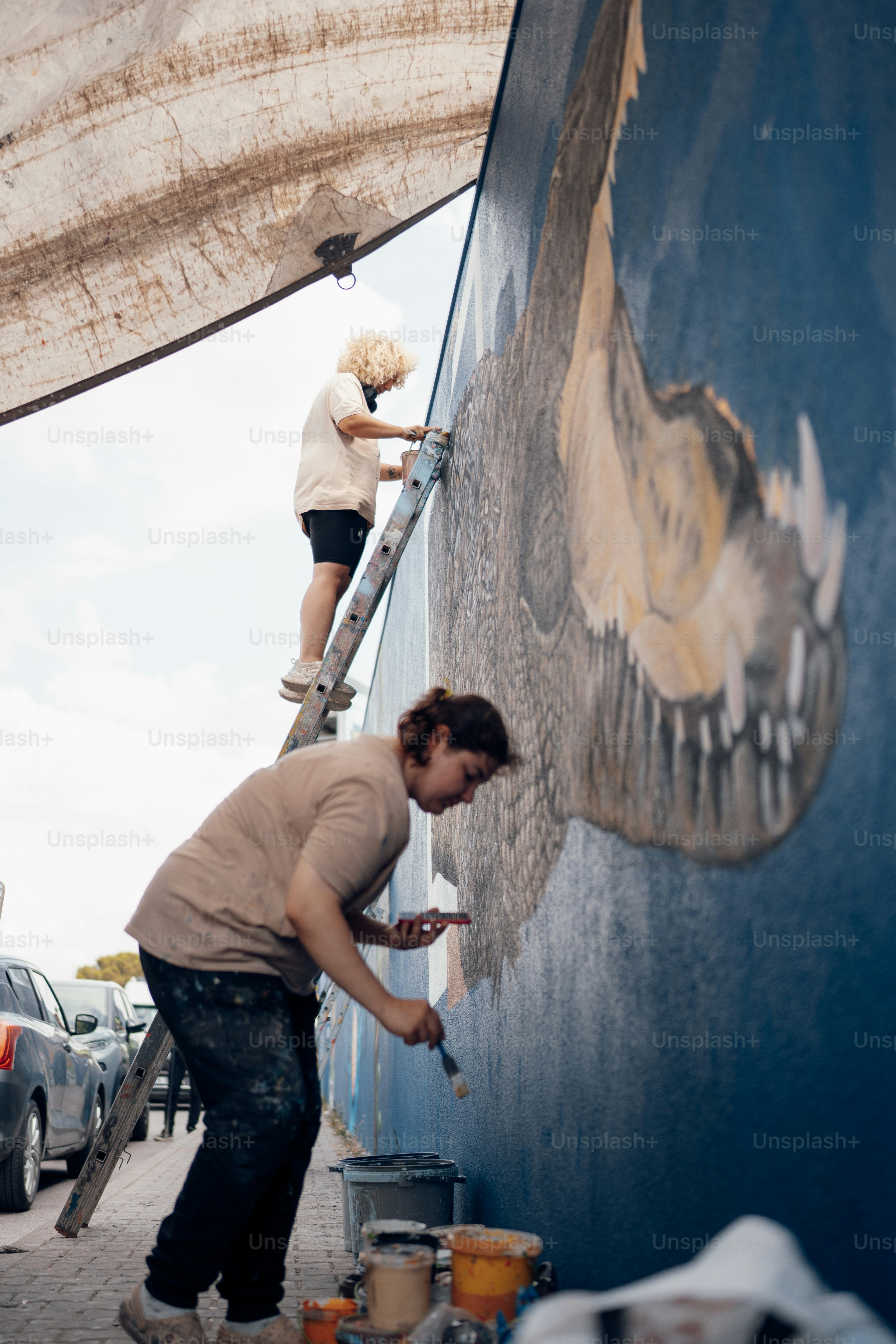 A man painting a mural on the side of a building photo – Graffiti Image ...