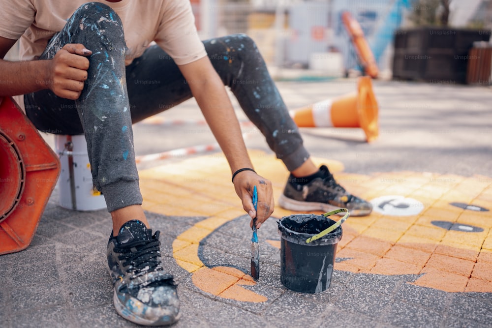 a man sitting on the ground next to a bucket of paint