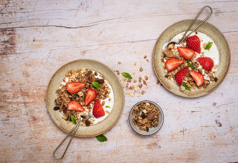 two bowls of granola and strawberries on a table