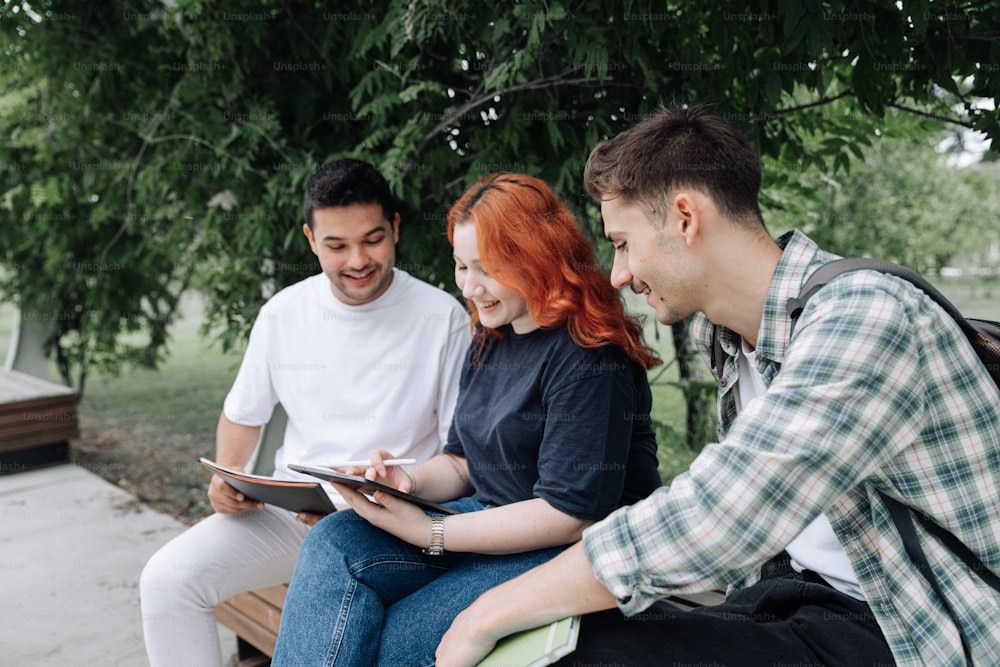 three people sitting on a bench looking at a tablet