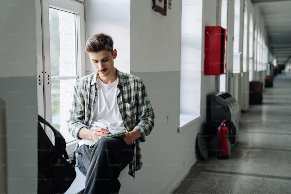 Ein junger Mann, der auf einem Fensterbrett sitzt und auf sein Handy schaut