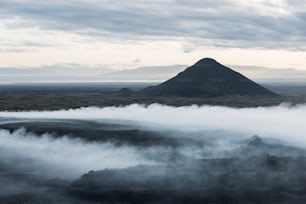 a mountain covered in fog with a mountain in the background