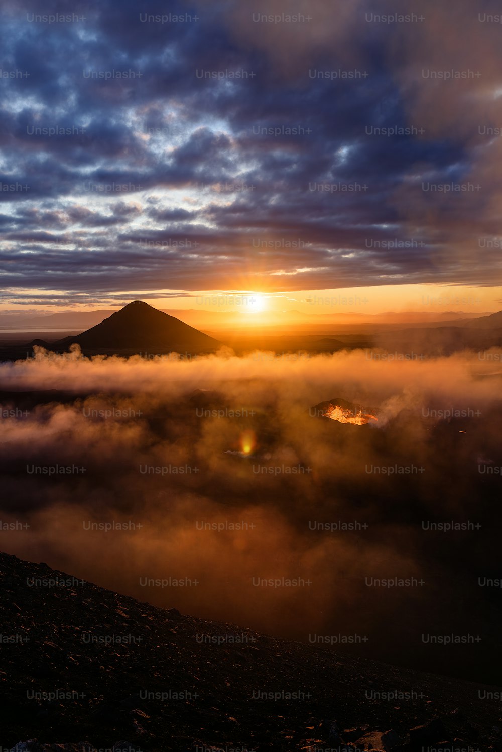 the sun is setting over a mountain covered in clouds