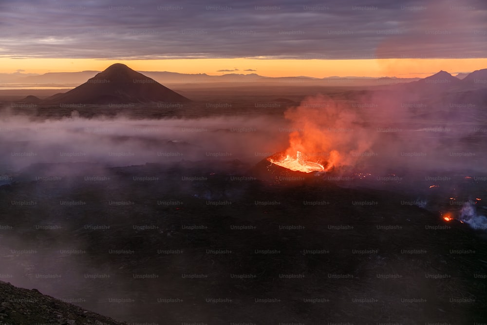 a volcano erupts lava as the sun sets