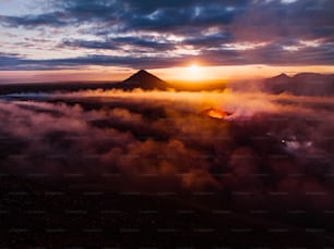 the sun is setting over a mountain covered in clouds