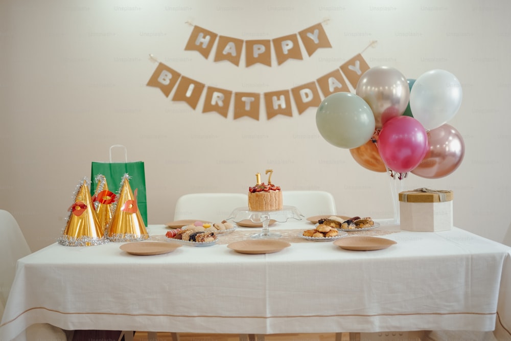 a white table topped with a cake and lots of balloons